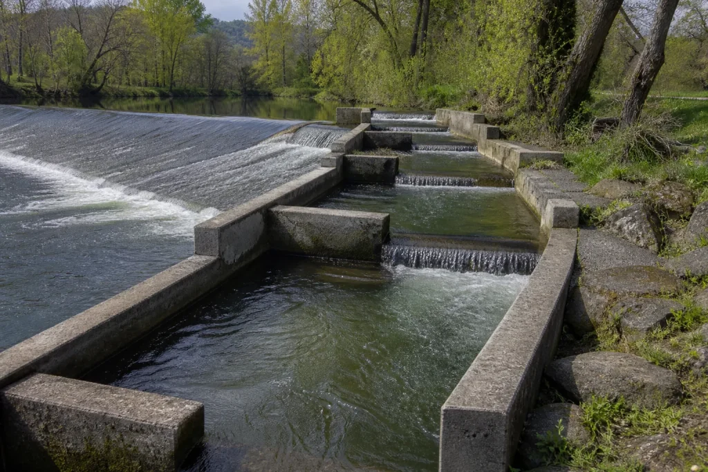 Ancien seuil de moulin en pierre partiellement démoli, avec une passe rustique en enrochements sur une petite rivière