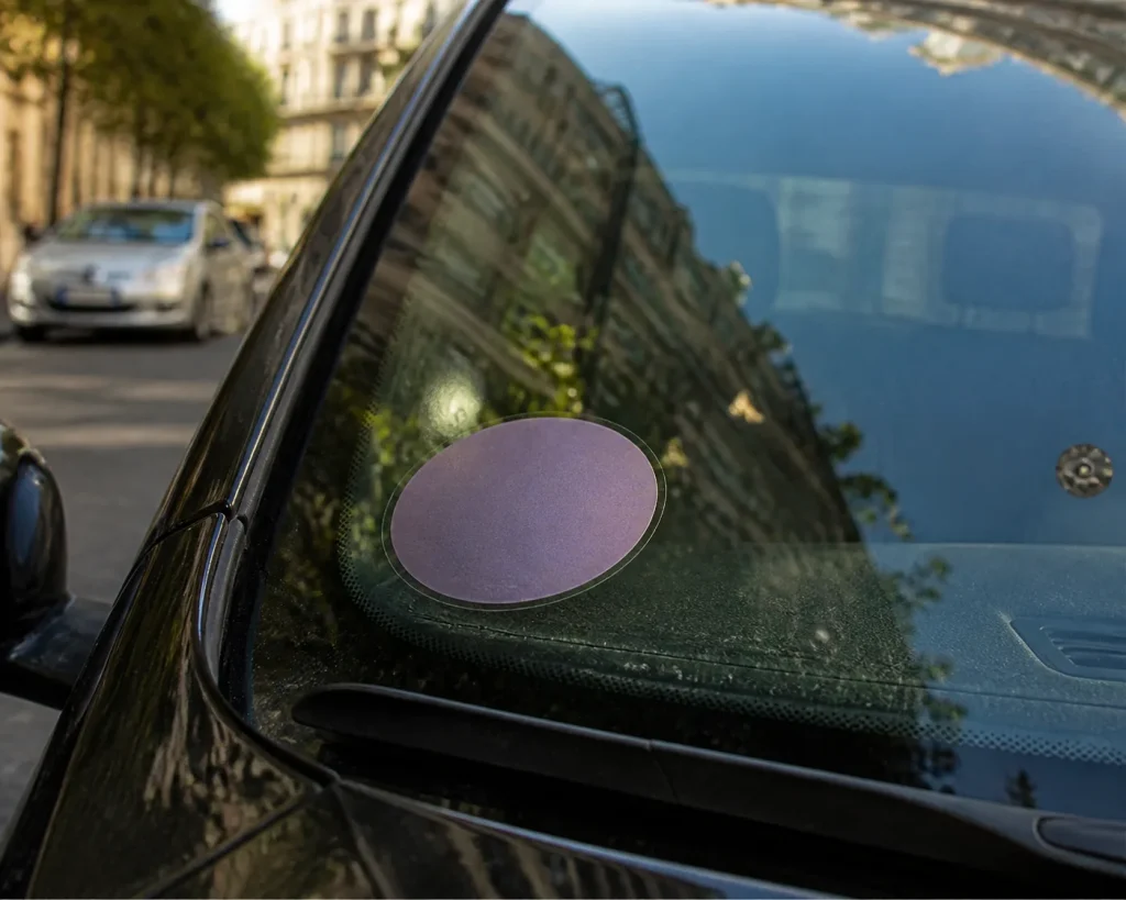 Vignette Crit'Air collée sur le pare-brise d'une voiture, vue de près depuis l'extérieur.