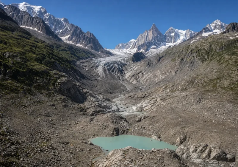 Langue glaciaire en recul dans les Alpes françaises, moraines grises et lac de fonte au premier plan.